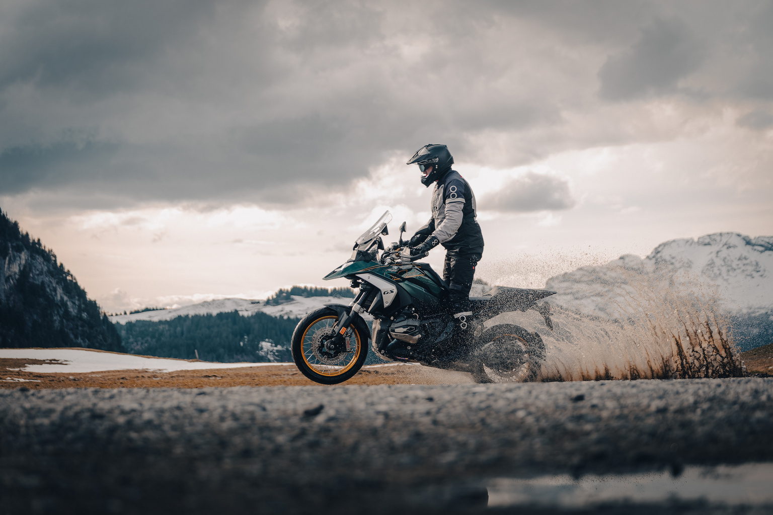 Motard en action projetant une gerbe d'eau, montagnes enneig&eacute;es.