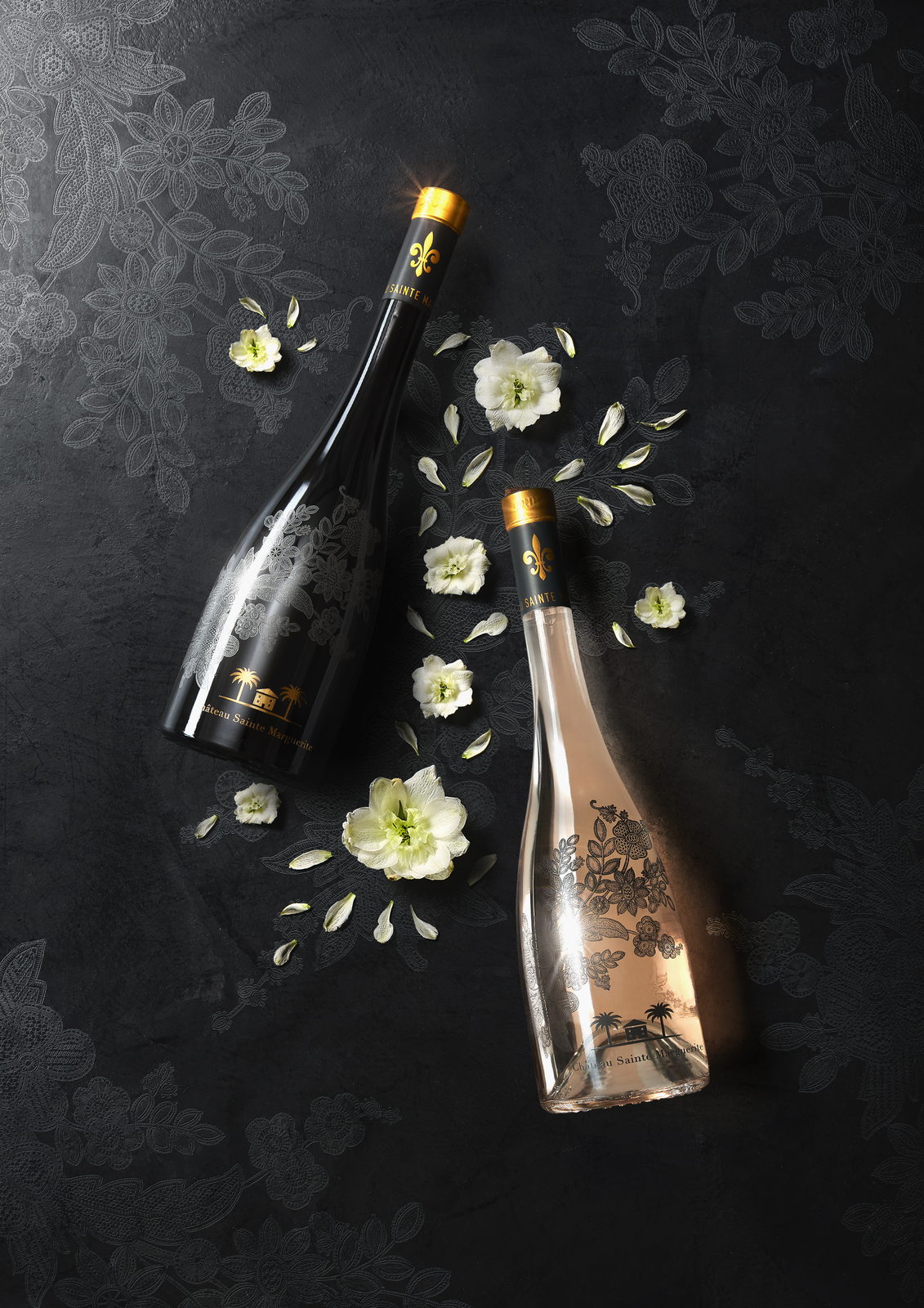 Deux bouteilles et fleurs blanches sur fond noir.